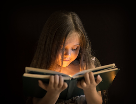 little cute girl is reading a magic book