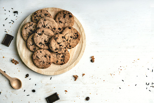 Stack of homemade chocolate chips cookies with glass of milk on a rustic wooden table
