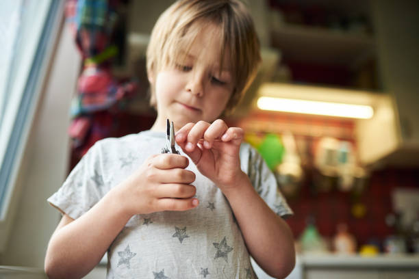 6 year old boy creates crafts at home. He is holding a plier and a wooden stick 6 year old boy creates crafts at home. He is holding a plier and a wooden stick. piler stock pictures, royalty-free photos & images
