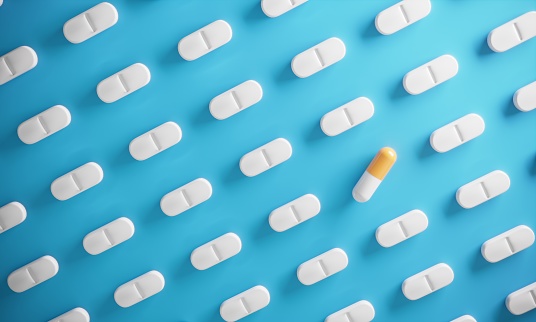 Orange-white colored capsule standing out from the crowd of pills on blue background ( 3d render )