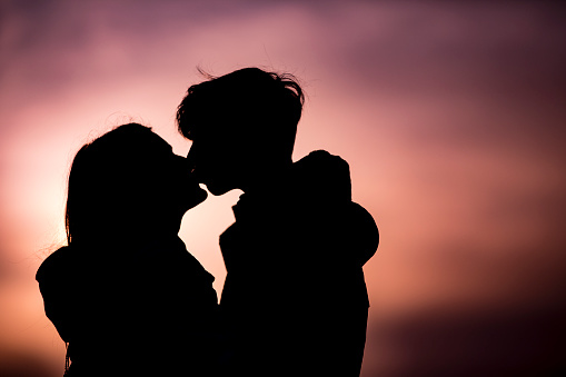 Teenage Couple Kissing at Sunset Outdoors.