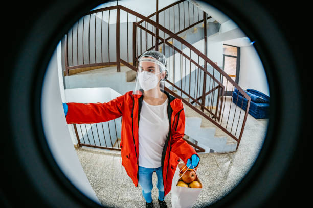 Woman delivering groceries during lockdown Woman with protective gloves and face mask at door of apartment delivering fresh food in bag during covid-19 coronavirus crisis curfew quarantine. peep hole stock pictures, royalty-free photos & images