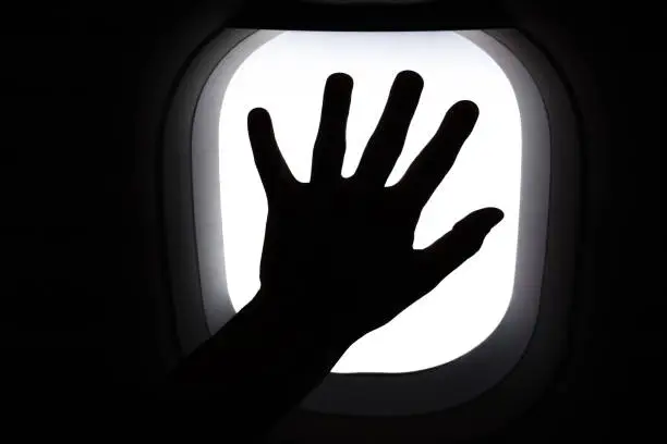 Travel by airplane. Hand on window airplane. Silhouette of hand on window during flight. Missing travel due to COVID-19 pandemic. Memoirs of traveling. Passengers hand on window of airplane