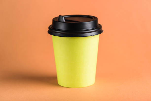 istock A green paper reusable coffee Cup with a closed black lid on an orange background. 1222756330