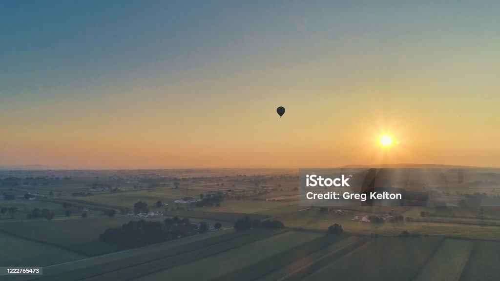 Aerial view of a summer sunset over farm lands with blue skies and red sun Aerial view of a summer sunset over farm lands with blue skies and red sun and a hot air balloon floating by Aerial View Stock Photo