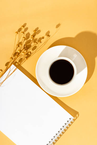 istock Top view sunny orange desktop with a blank notebook and a cup of coffee. 1222767897