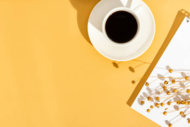 Top view sunny orange desktop with a blank notebook and a cup of coffee.
