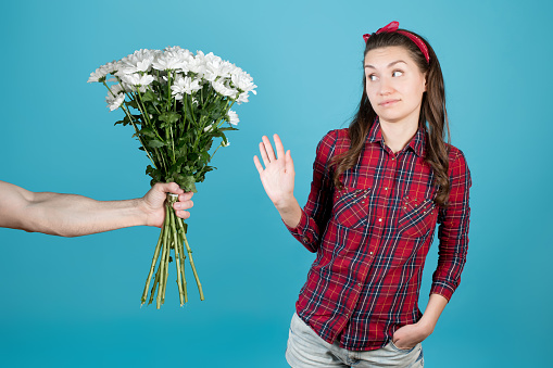 A country girl in a red plaid shirt carefully refuses flowers. Male hand holds out a bouquet of white chrysanthemums to a girl