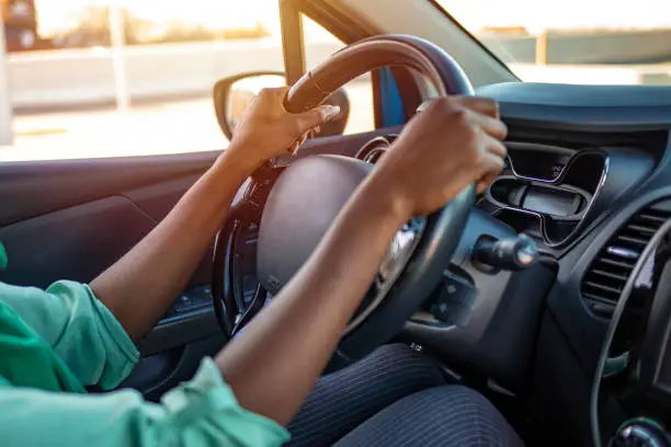 Side view of a woman sitting in a car holding a steering wheel and looking on the road. Young African American woman driving the car. Cropped shot of an unrecognizable woman driving her car