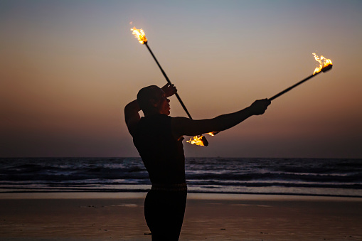 Goa, India, February 9, 2019: Fire juggler performing with fire sticks on the beach in Arambol