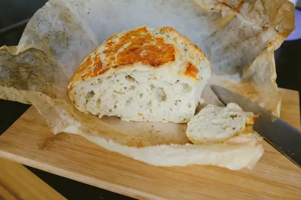 April 29, 2020 - Warsaw, Poland: freshly baked homemade bread cut and sliced with a knife lying on a wooden cutting board and wax paper still warm