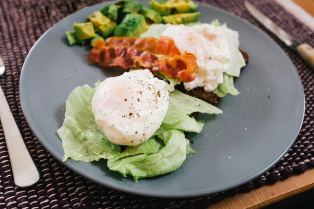 istock Poached eggs on wholegrain toasted bread, iceberg lettuce, avocado, bacon on a blue plate - eggs Benedict sandwich with vegetables ready-to-eat, close-up 1222773320