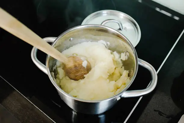 April 30, 2020 - Warsaw, Poland: mashing potatoes in a cooking pan - freshly cooked potatoes and wooden masher on a kitchen stove