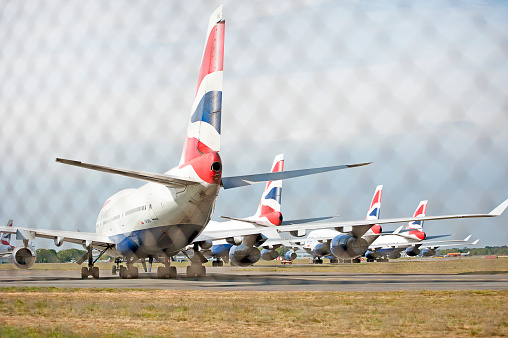 Boeing 747-400 series aircraft, Bournemouth Hurn Airport, Dorset, England, UK. Redundant British Airways Jumbo Jets parked on the perimeter track of Bournemouth Hurn Airport, seen through chain-link fencing during Coronavirus lockdown, when the virus grounded all international aircraft and travel.