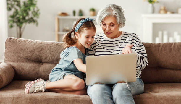 bambina con nonna che usa laptop a casa - wireless technology cheerful granddaughter grandmother foto e immagini stock