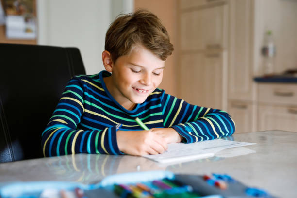 istock Hard-working happy school kid boy making homework during quarantine time from corona pandemic disease. Healthy child writing with pen, staying at home. Homeschooling concept 1222781851
