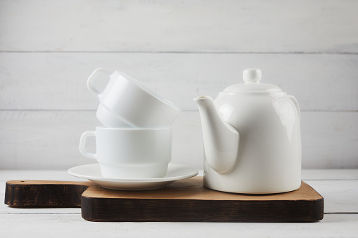 Cup of tea, teapot, oak cutting board on white wooden background. Rustic style