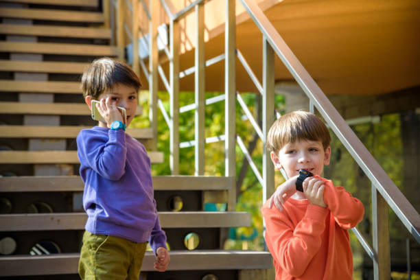 istock Two friends calling each other while standing on stairs outdoor. One boy has mobile phone, other has smart watch with GPS. Protection and safe communication with children concept 1222784985