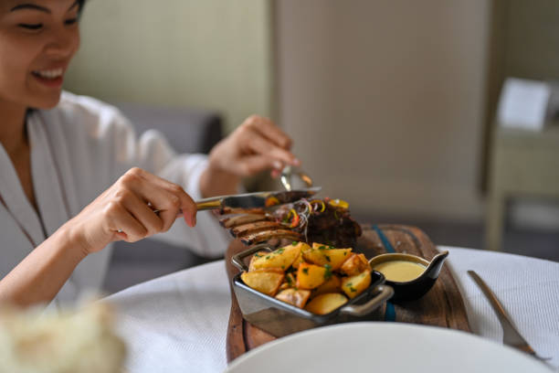 Beautiful asian woman having lunch hotel room, eating lamb ribs with baked potatoes, she is wearing bathrobe, Nikon Z7
