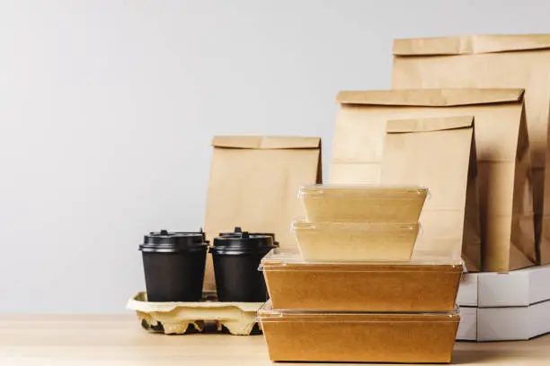 Photo of Many various take-out food containers, pizza box, coffee cups and paper bags on light grey background