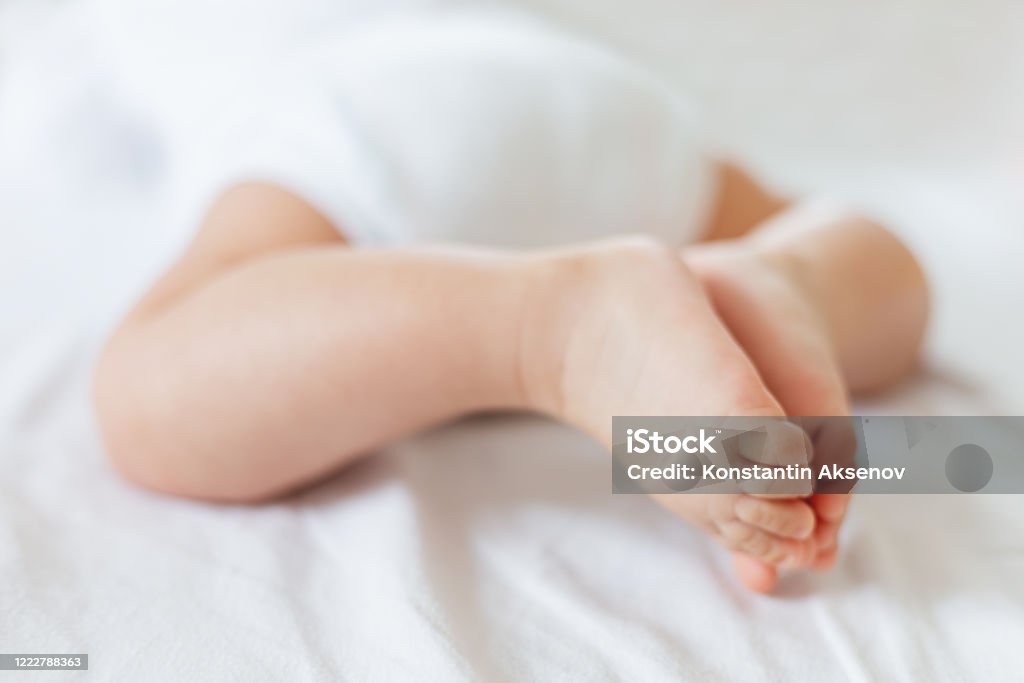 Baby's feet. Bare heels of little child wearing white bodysuit and diaper. Cozy morning bedtime at home. Buttocks Stock Photo