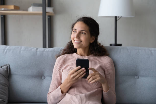 istock Distracted young smiling woman resting on sofa, holding smartphone. 1222788518