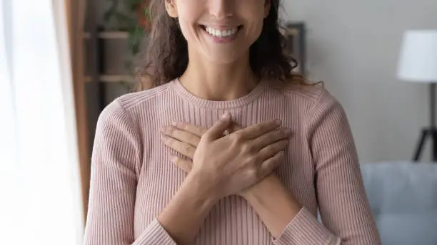 Photo of Close up happy sincere female holding folded hands on chest.