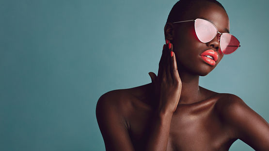 African female model wearing funky sunglasses. looking away. Stylish woman with buzzcut on grey background.