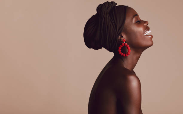 Fashionable african woman smiling on beige background Side view of fashionable african woman smiling on beige background. African female with a turban smiling in studio. shaved black women stock pictures, royalty-free photos & images