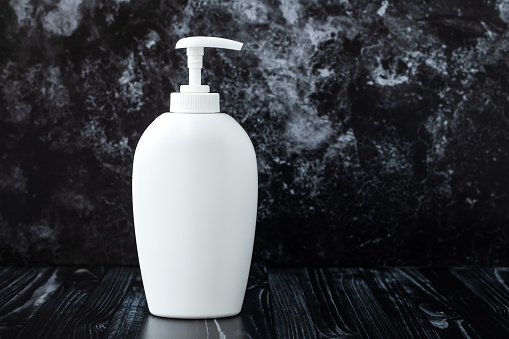 White liquid soap on black marble background in bathroom. Concept of hygiene. Dispenser plastic bottle. Text, copy space. Product of cosmetic