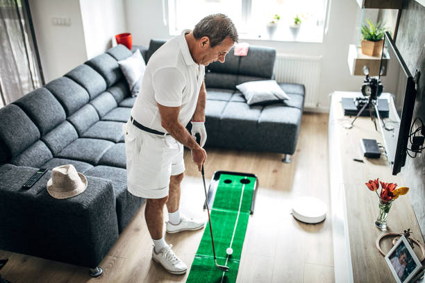 senior mann spielt minigolf im wohnzimmer - retirement golfer happiness relaxation stock-fotos und bilder