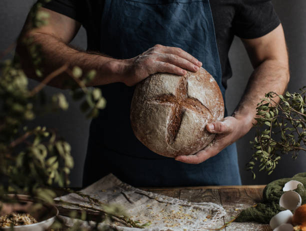 las manos del panadero sostienen una hogaza de pan de centeno - bakers yeast fotografías e imágenes de stock