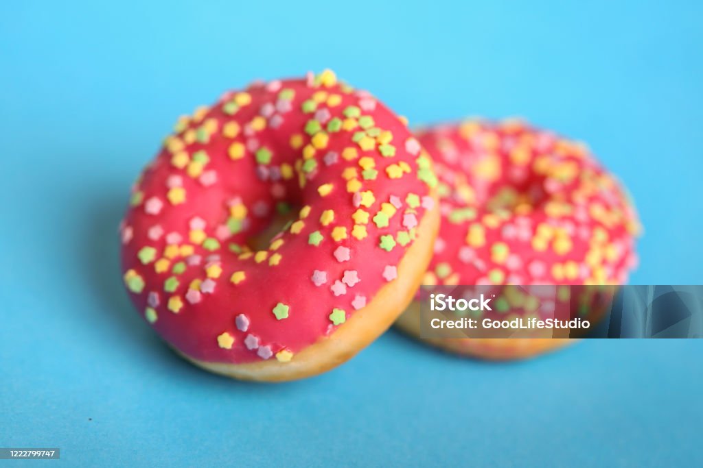 Delicious pink glazed donuts American style donuts with pink glazing and colorful star shaped sprinkles on blue background. American Culture Stock Photo