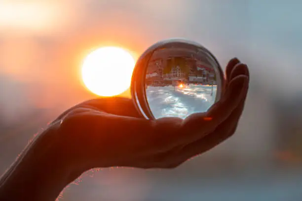 Photo of Sun and glass ball in hand, man holding crystal ball, crystal lens with sun rays and city as reflection