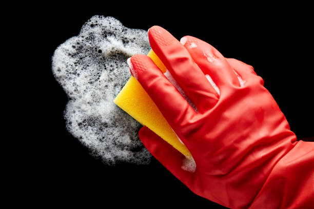 istock Human hand in a red rubber glove wiping with a sponge on isolated black background 1222801675