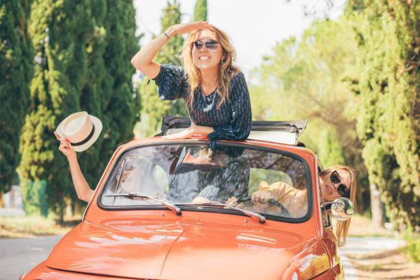 Three girls best friends enjoying summer trip in Tuscany with red vintage car stock photo