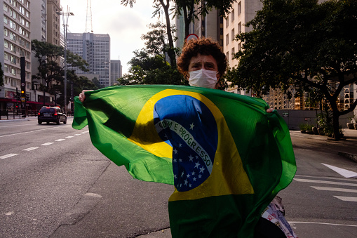 Sao Paulo, Brazil - April 11, 2020: Woman wearing protective face mask, selling Brazilian flags on the Paulista Avenue.