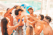Multiracial group of young friends toasting at summer pool party, drinking champagne or wine and having fun together