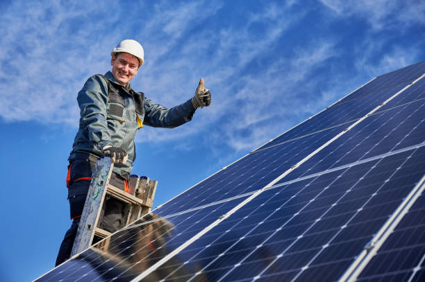 trabajador masculino en la planta solar instalando baterías solares, de pie en una escalera en un día soleado - solar panel engineer solar power station solar energy fotografías e imágenes de stock