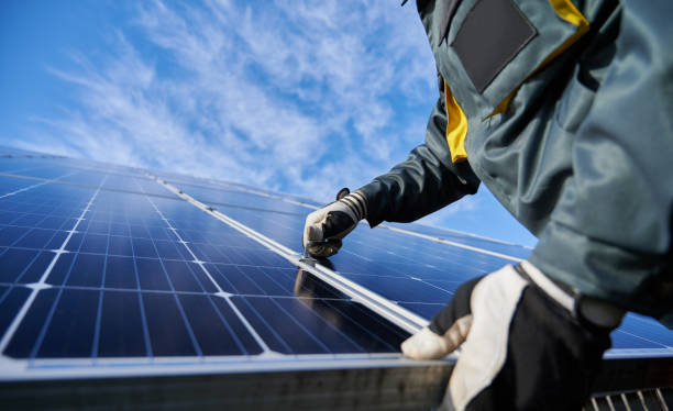 Male worker repairing photovoltaic solar panel. Close up of man technician in work gloves installing stand-alone photovoltaic solar panel system under beautiful blue sky with clouds. Concept of alternative energy and power sustainable resources. rooftop solar stock pictures, royalty-free photos & images