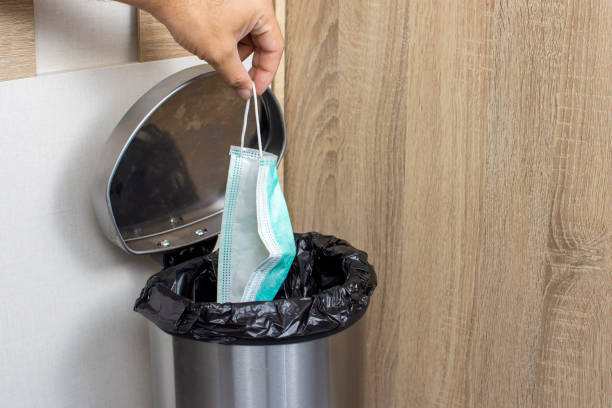 istock Disposable medical masks in a hand let down to infectious waste trash bin. 1222814599