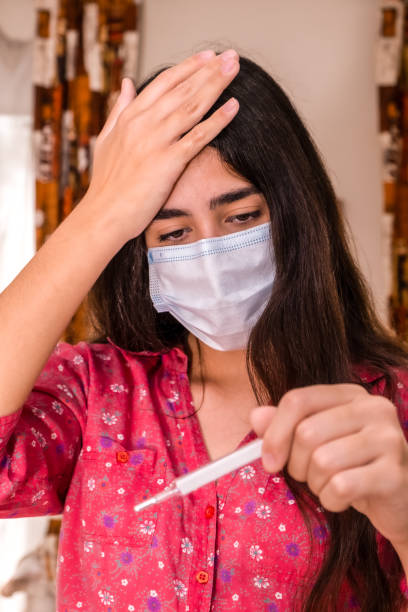 istock Young woman wearing a mask takes her temperature with a thermometer 1222816596