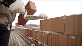 Worker puts a brick wall. Bricklayer working in construction site of a brick wall. Bricklayer putting down another row of bricks in site