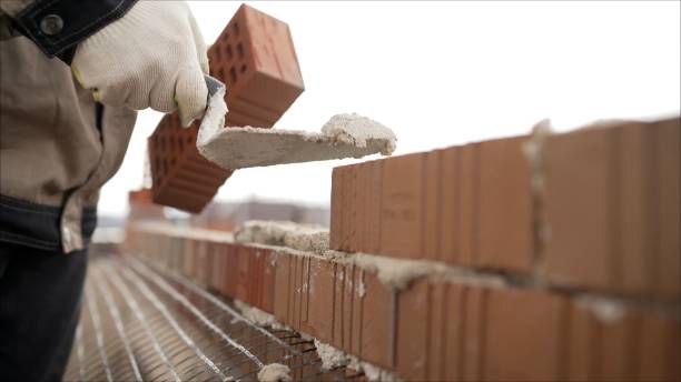Worker puts a brick wall. Bricklayer working in construction site of a brick wall. Bricklayer putting down another row of bricks in site stock photo