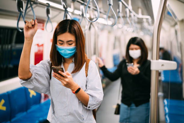 Young asian woman wearing protective face mask using smartphone in underground train due to the polluted air or pm 2.5 and Coronavirus or COVID-19 outbreak situation in all of landmass in the world. Young asian woman wearing protective face mask using smartphone in underground train due to the polluted air or pm 2.5 and Coronavirus or COVID-19 outbreak situation in all of landmass in the world. landmass stock pictures, royalty-free photos & images