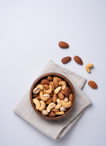 Nuts almonds, pistachios and cashews are placed in a wooden bowl on a linen napkin on a light blue background. Top view and copy space. Vertical orientation