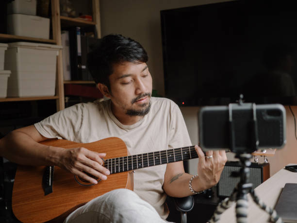 istock Asian man learning to playing guitar in room at home 1222822998