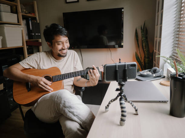Asian man learning to playing guitar in room at home