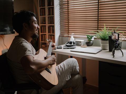 Asian man playing music together through a video call on the internet. Music band repetition online. Having fun while staying at home.
