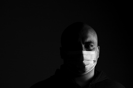 Caucasian young man with medical protective face mask illustrates pandemic coronavirus, Covid 19 disease isolated on black copy space. Covid-19 outbreak, flu contamination and healthcare concept